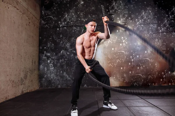 Man with battle ropes exercise in the fitness gym