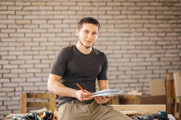 Man carpenter in his home studio draws sketches in pencil in notebook — Stock Photo, Image