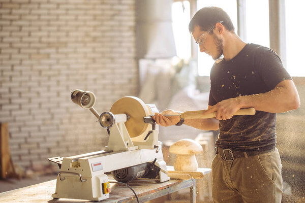 man working at small wood lathe, an artisan carves piece of wood