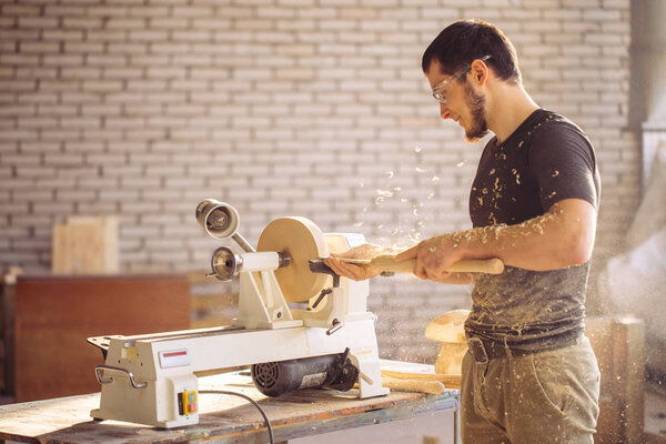man working at small wood lathe, an artisan carves piece of wood