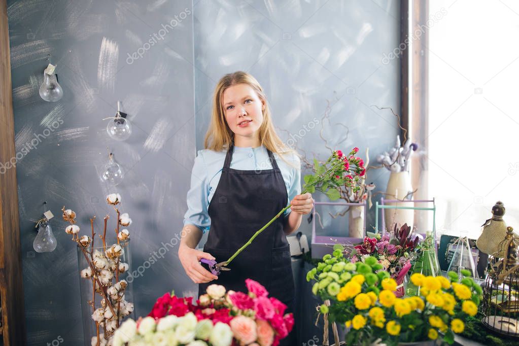 young woman holding long flower and cutting it at florist shop