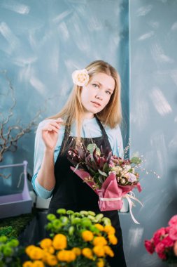 çiçek tabloyla önünde duran ve kameraya bakıyor güzel sarışın kız