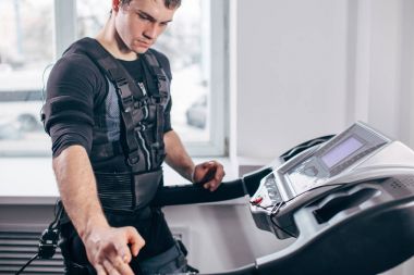 Man in black suit for ems training running on treadmill at gym clipart