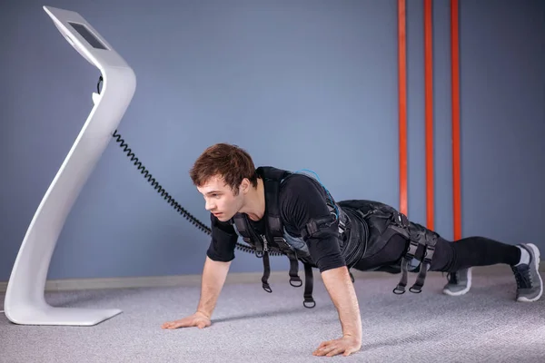 Человек в электрических мышечных стимуляционных костюмах делает упражнения на доске. EMS — стоковое фото
