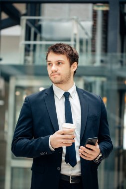 kahve fincanı tutarak ve koridorda yürürken akıllı telefonunu kullanarak kendine güvenen adam