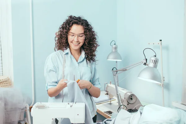 Kleermaker kijken naar blauwe stof in haar armen op het werk — Stockfoto