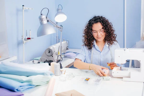 Nice tailor is sitting at desk and touching pink thread — Stock Photo, Image