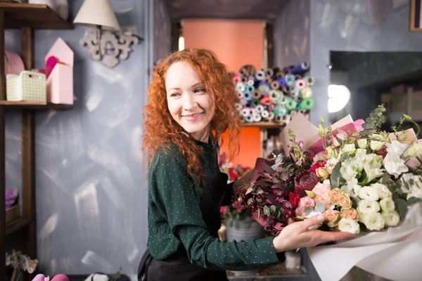 Kvinna med rött hår håller blommor och tittar åt sidan blomsteraffär — Stockfoto