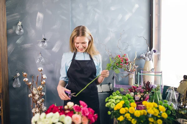 Girl looking at flower and cutting it in front of gorgeous flowers — Stock Photo, Image