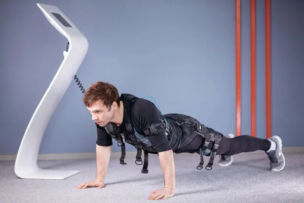 Человек в электрических мышечных стимуляционных костюмах делает упражнения на доске. EMS — стоковое фото