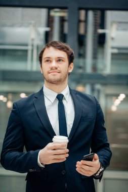 kahve fincanı tutarak ve koridorda yürürken akıllı telefonunu kullanarak kendine güvenen adam
