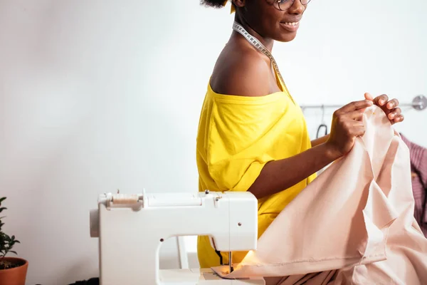 Mulher africana costureira olhando para tecidos rosa e de pé na oficina — Fotografia de Stock