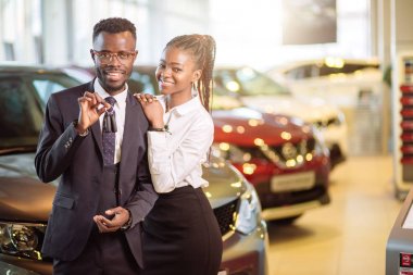 Visiting car dealership. couple holding key of their new car, looking at camera clipart