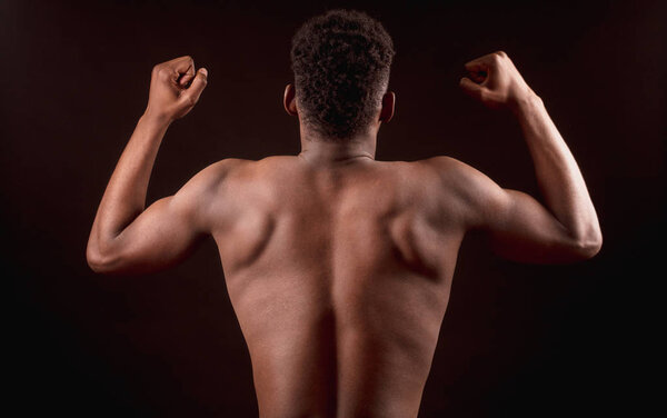 Back view image of Afro american strong male bending elbows the biceps with clenched fists. strong constitution of body. performing bodybuilding pose