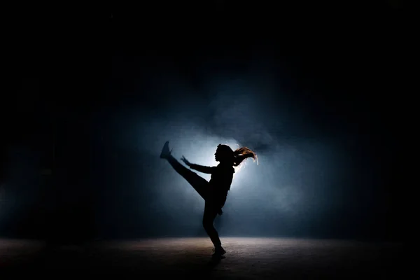 Jeune danseuse aux cheveux longs levant la jambe sur scène sombre — Photo