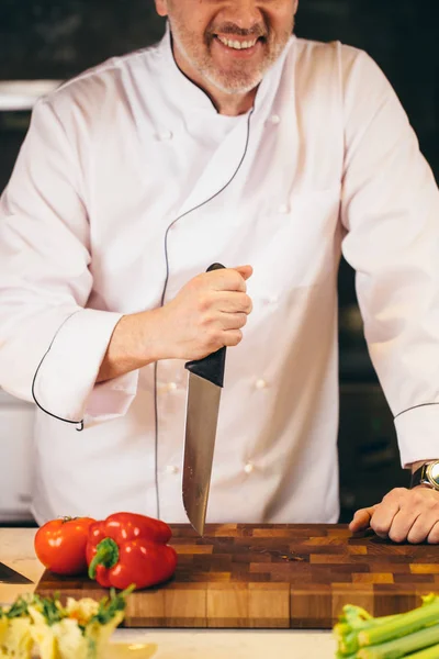 Closeup bijgesneden schot van lachende oude kok houden het mes op de snijplank — Stockfoto