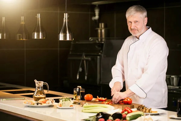 Mavi gözlü gri saçlı yaşlı aşçı mutfakta çalışıyor — Stok fotoğraf
