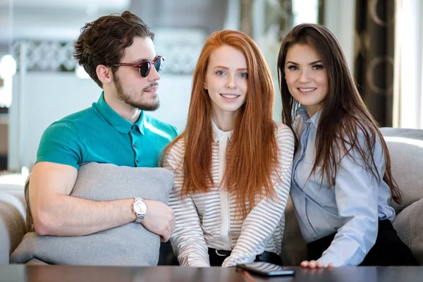 Young man in glasses with cusion in hands looking at two good-looking women. — Stock Photo, Image