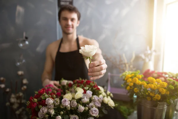 Foto borrosa del hombre mostrando rosa blanca a la cámara en el mercado de flores — Foto de Stock