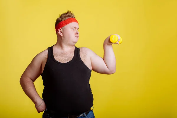 黄色の背景のダンベルのデブ男。太っている人のための動機 — ストック写真