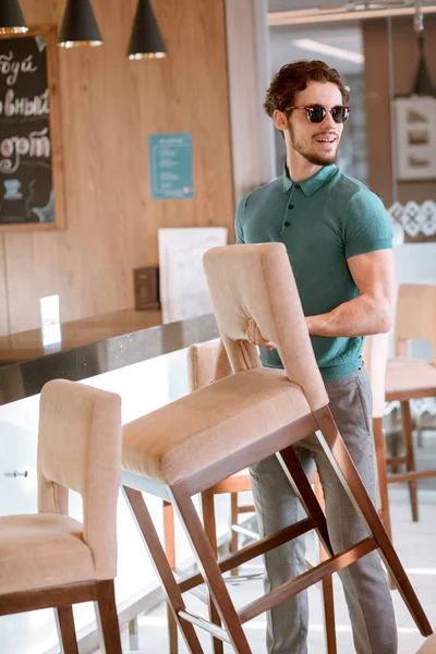 Hombre con gafas y camiseta azul y pantalón gris con silla . — Foto de Stock
