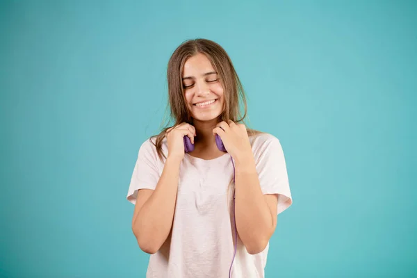 Adolescente sonriente con el pelo largo y liso de color marrón se está quitando los auriculares azules — Foto de Stock