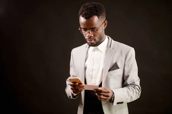 Homem africano segurando folha de papel e telefone inteligente e discando um número — Fotografia de Stock