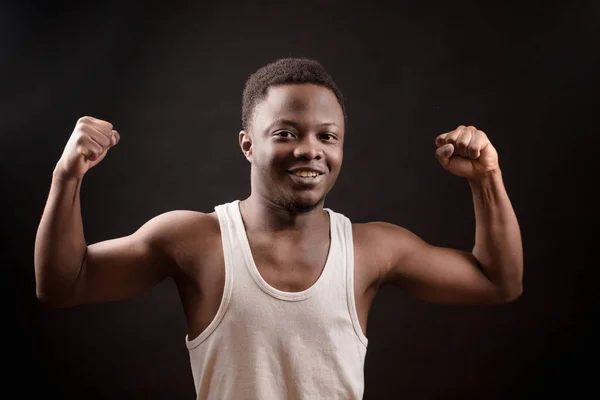 Afro sportsman is giving biceps a flex on the black background.