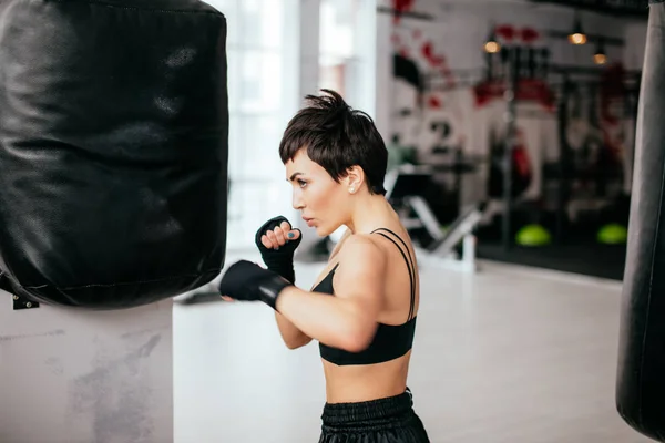 Jeune femme améliore les compétences de boxe avec un énorme sac de boxe noir — Photo