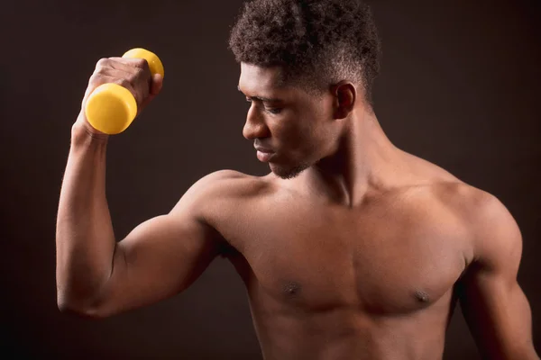 Självsäker afrikanska man träning med gula dum-bell på den svarta bakgrunden — Stockfoto