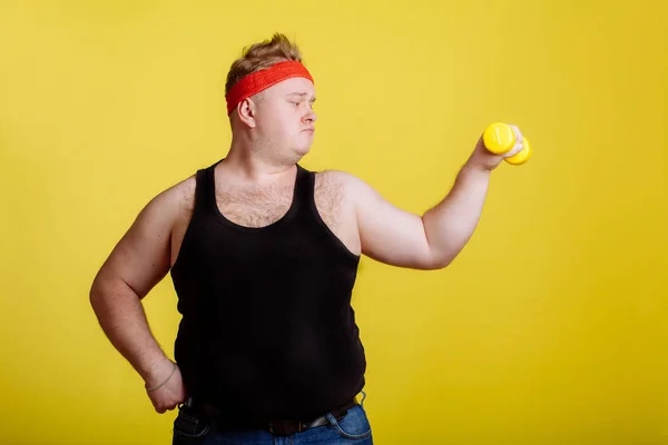 黄色の背景のダンベルのデブ男。太っている人のための動機 — ストック写真