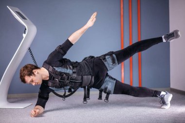 yan tahta egzersiz yaparak elektrik kas stimülasyonu elbiseli adam. EMS