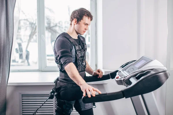 Man in black suit for ems training running on treadmill at gym