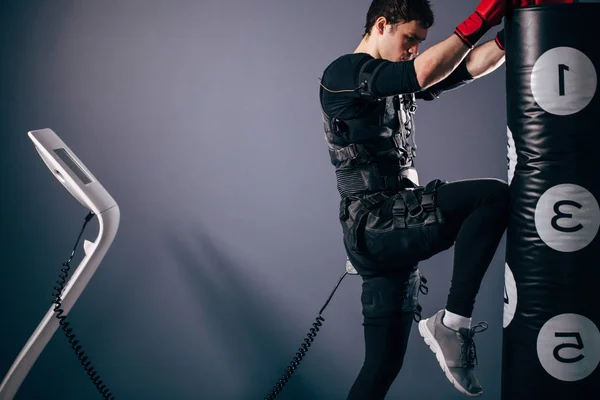Hombre entrenando patada de rodilla. Un kickboxer con traje de estimulación eléctrica —  Fotos de Stock