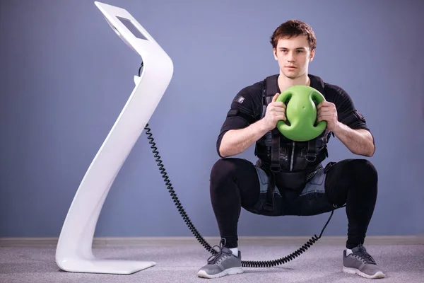 Man in electric muscular suit to stimulate with training medecine ball