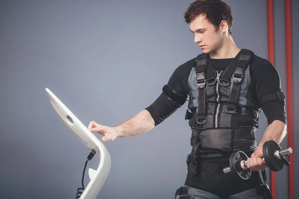 Mannen i elektrisk muskulär stimulering kostym står med hantlar — Stockfoto