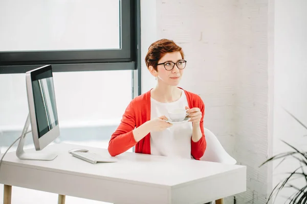 Zakenvrouw zittend op Bureau met een kopje koffie aan tafel met computerscherm — Stockfoto