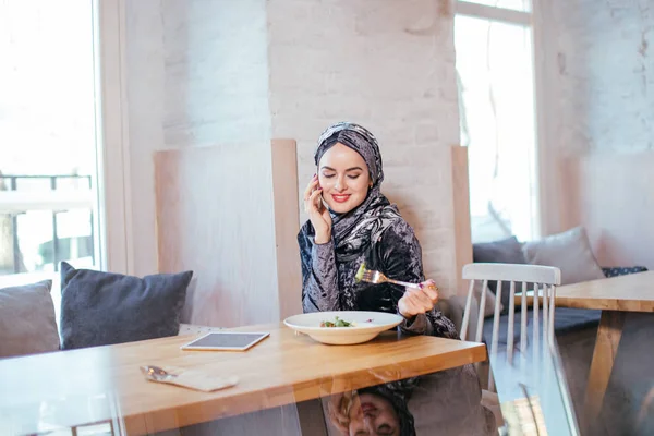 Joven mujer musulmana hablando por teléfono en la cafetería y mirando en la ventana — Foto de Stock