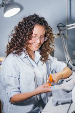 Genç kadın tasarımcı atölyesinde masada mavi kumaş kesme kıvırcık saçlı