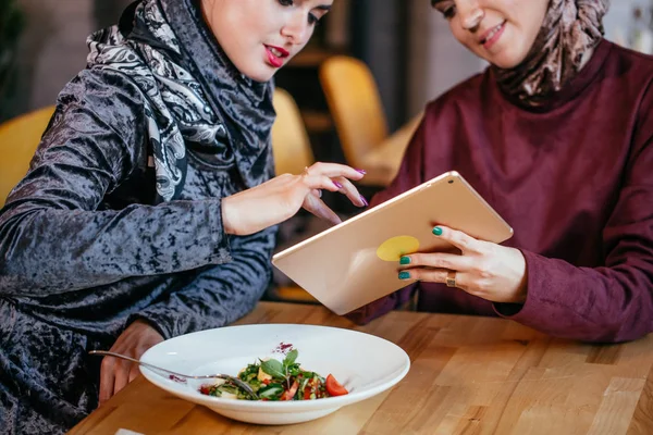 Dos mujeres musulmanas en la cafetería, comprar en línea usando tableta electrónica — Foto de Stock