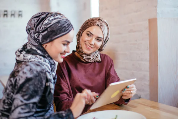 Two Muslim women in cafe, shop online using electronic tablet — Stock Photo, Image
