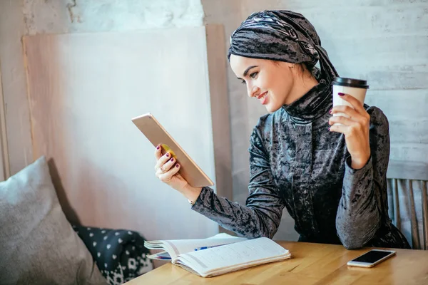 Wanita muslim bekerja dengan tablet dan minum kopi di kafe — Stok Foto