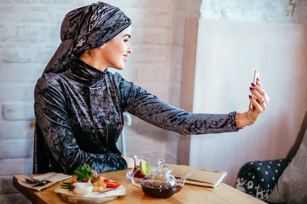 Мусульманка делает селфи в кафе со смартфоном — стоковое фото