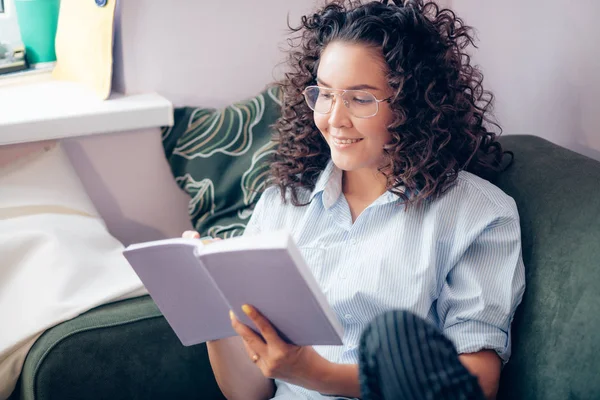 woman with curly hair in casual clothers reading book at home