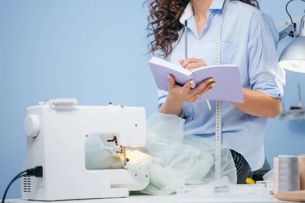 Знімок жінки, що робить нотатки поруч зі швейною машиною — стокове фото