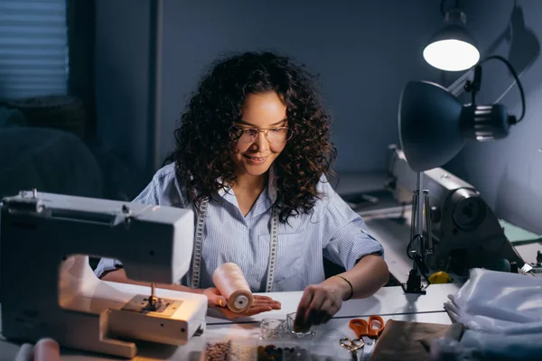 Dressmaker está enhebrando cuentas delante de la máquina de coser en la habitación negra — Foto de Stock