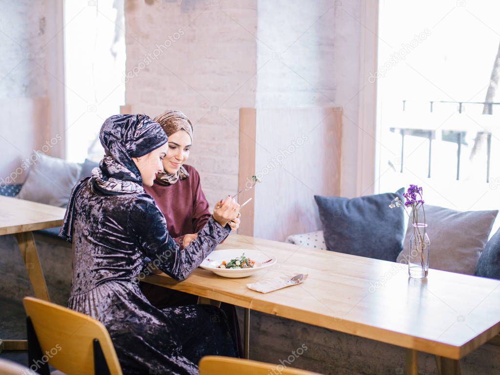 Two Muslim women in cafe, shop online using electronic tablet