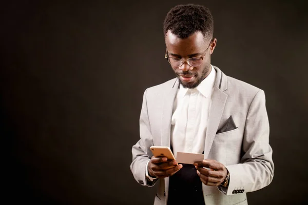 Imagem de perto do gerente Africano olhando para o seu cartão de visita e telefone celular — Fotografia de Stock