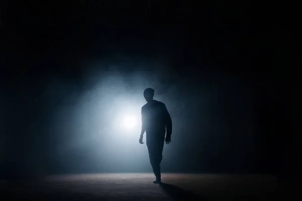dark silhouette of slim man walking on the street at night