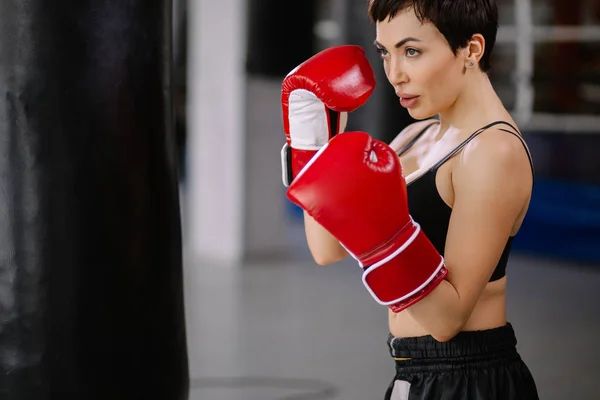 Mujer con elegante figura golpeando una bolsa de boxeo mirada seria — Foto de Stock